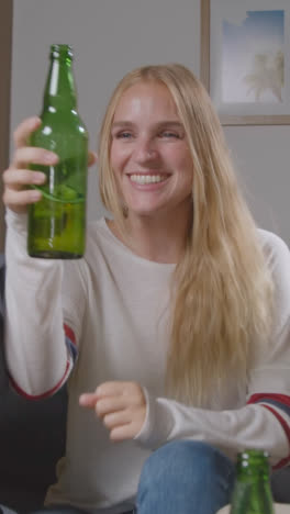 Vertical-Video-Of-Multi-Cultural-Friends-Celebrating-Watching-Sports-Game-On-TV-Sitting-On-Sofa-At-Home-Drinking-Beer